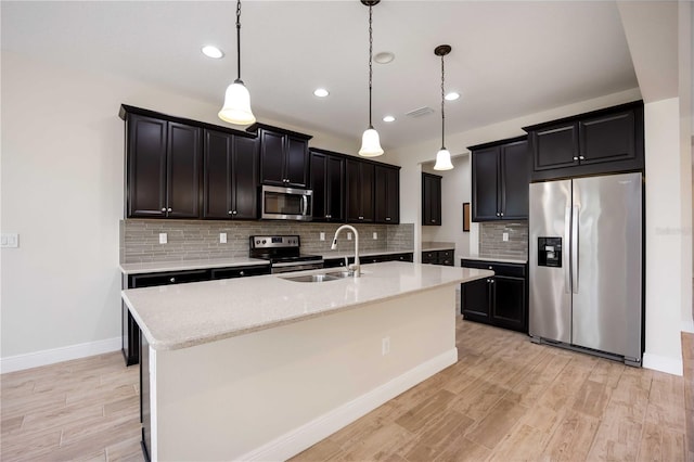 11680 Tapestry Ln, Venice, FL 34292 - kitchen with appliances with stainless steel finishes, light wood-style flooring, backsplash, pendant lighting, and a kitchen island with sink