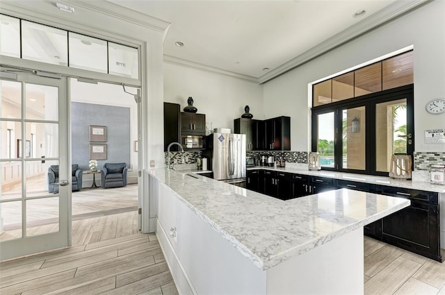 11680 Tapestry Ln, Venice, FL 34292 - kitchen with stainless steel appliances, dark cabinetry, light stone countertops, decorative backsplash, and crown molding