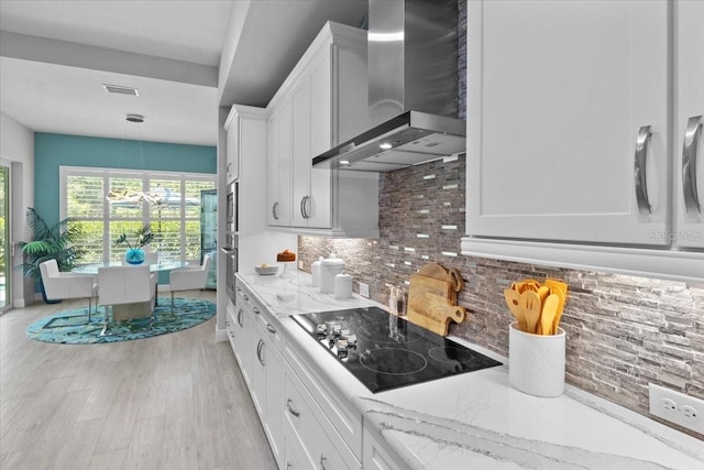 3605 Wild Blossom Pl, Parrish, FL 34219 - kitchen with wall chimney range hood, appliances with stainless steel finishes, light wood-style flooring, decorative backsplash, and white cabinets