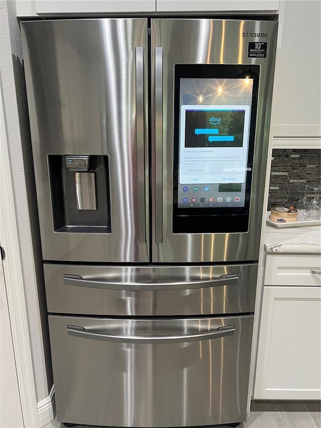 3605 Wild Blossom Pl, Parrish, FL 34219 - kitchen view of stainless steel fridge, white cabinetry, decorative backsplash, and light stone counters