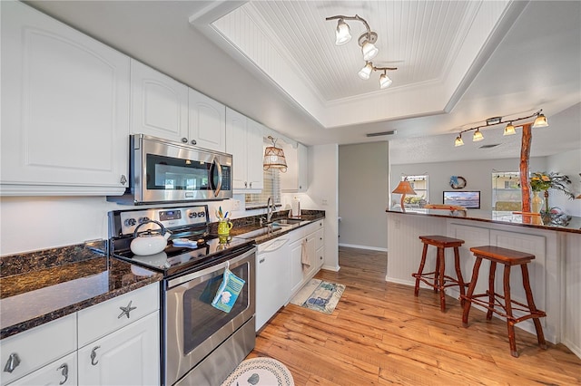 7216 11th Ave W Unit 203, Bradenton, FL 34209 - kitchen featuring stainless steel appliances, rail lighting, a tray ceiling, light wood-type flooring, and white cabinets