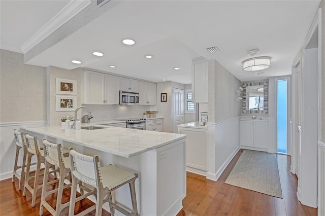 6480 Midnight Pass Rd Unit 211, Sarasota, FL 34242 - kitchen featuring a peninsula, a wainscoted wall, hardwood / wood-style floors, appliances with stainless steel finishes, and light stone counters