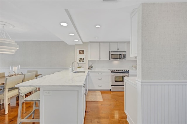 6480 Midnight Pass Rd Unit 211, Sarasota, FL 34242 - kitchen featuring a peninsula, appliances with stainless steel finishes, a breakfast bar area, light wood-style floors, and a wainscoted wall