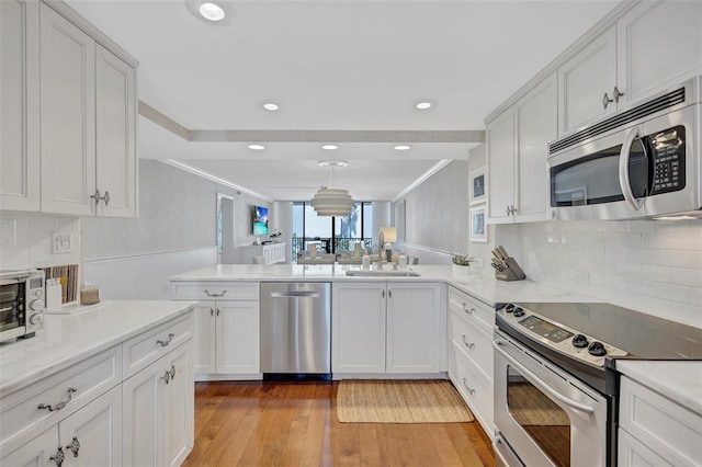 6480 Midnight Pass Rd Unit 211, Sarasota, FL 34242 - kitchen featuring appliances with stainless steel finishes, a peninsula, white cabinets, tasteful backsplash, and light wood finished floors
