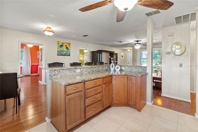 8606 Gold Pine Dr, Port Richey, FL 34668 - kitchen featuring a ceiling fan, light wood-style flooring, brown cabinets, light stone countertops, and a peninsula