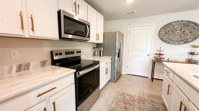 12293 Mountain Island Trl, Parrish, FL 34219 - kitchen with stainless steel appliances, white cabinets, light tile patterned floors, and light stone countertops