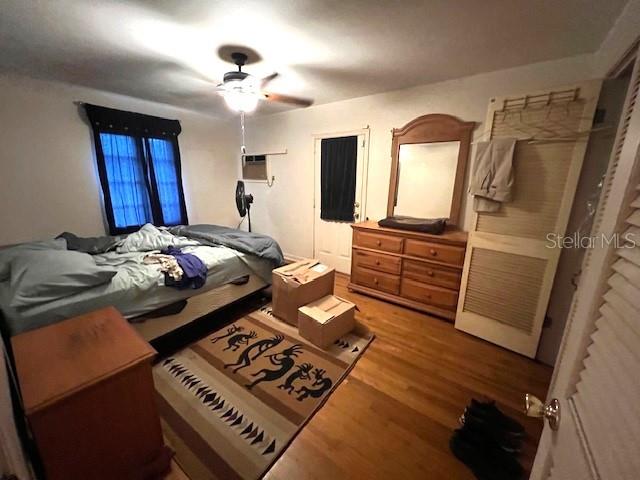 bedroom featuring a wall mounted air conditioner, wood-type flooring, and ceiling fan