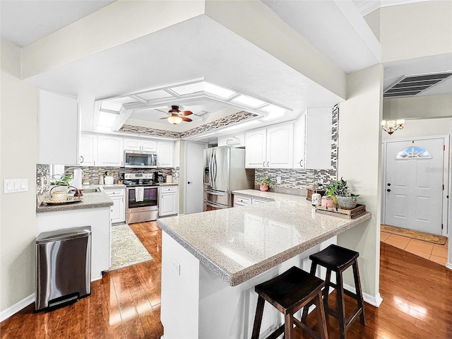 kitchen with ceiling fan with notable chandelier, stainless steel appliances, hardwood / wood-style flooring, and a breakfast bar