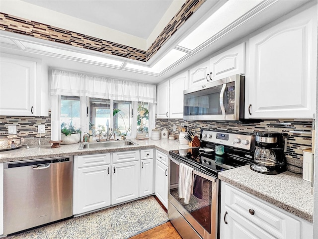 kitchen featuring appliances with stainless steel finishes, sink, tasteful backsplash, light wood-type flooring, and white cabinetry