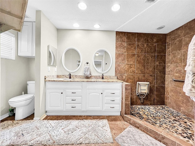 bathroom with tile floors, dual vanity, a tile shower, toilet, and a textured ceiling