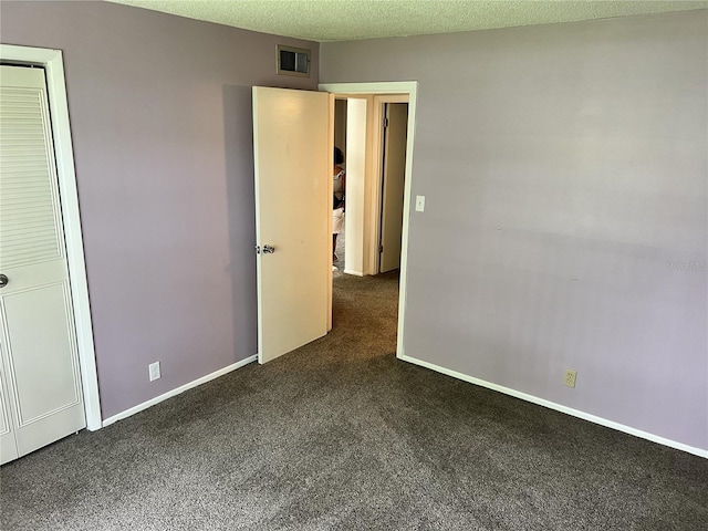 unfurnished bedroom featuring dark colored carpet, a textured ceiling, and a closet