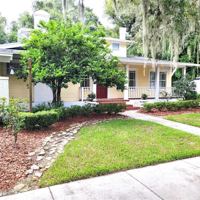 view of property hidden behind natural elements featuring a chimney, a porch, and a front yard