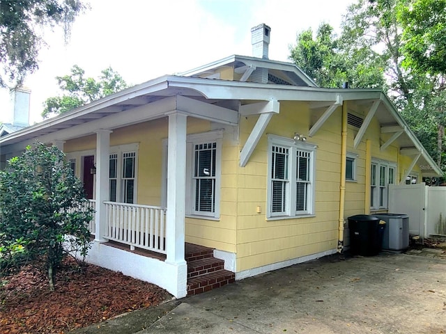 view of side of home with a chimney, fence, and a porch