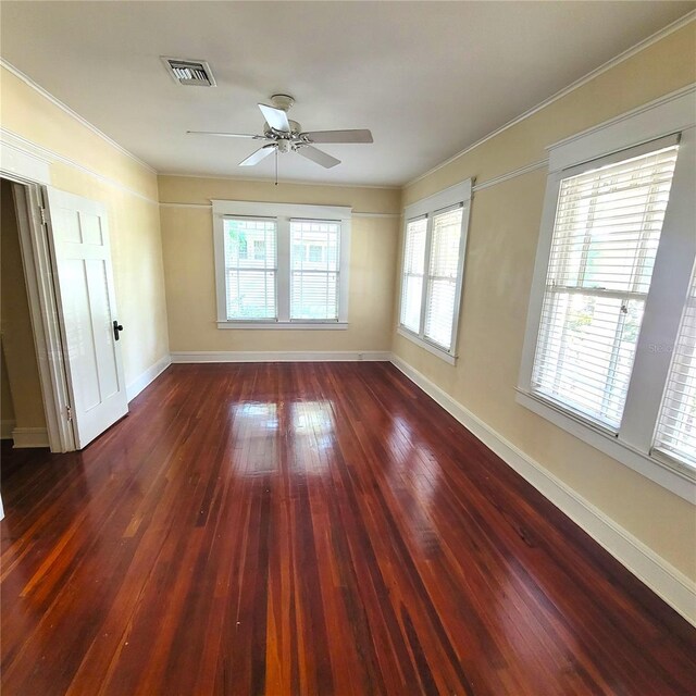 empty room with ornamental molding, visible vents, dark wood finished floors, and baseboards