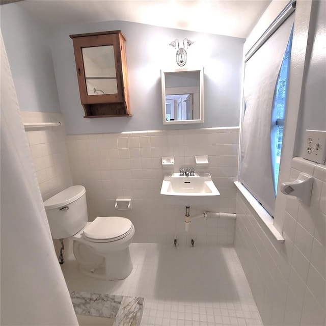 bathroom featuring a wainscoted wall, tile walls, toilet, a sink, and tile patterned floors