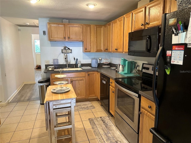 kitchen with a textured ceiling, light tile patterned flooring, a center island, and black appliances