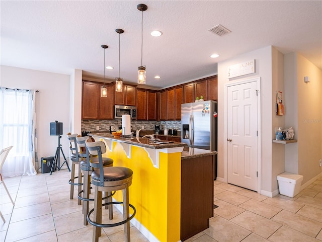 kitchen featuring appliances with stainless steel finishes, backsplash, a kitchen bar, pendant lighting, and dark stone counters