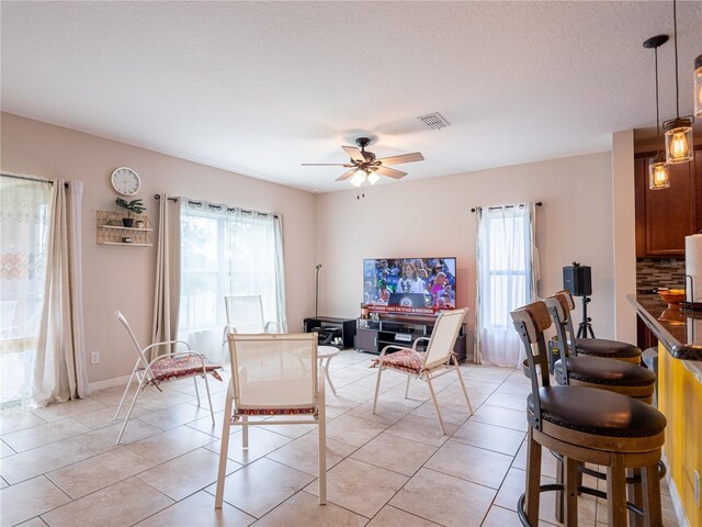 tiled dining area with a textured ceiling, plenty of natural light, and ceiling fan