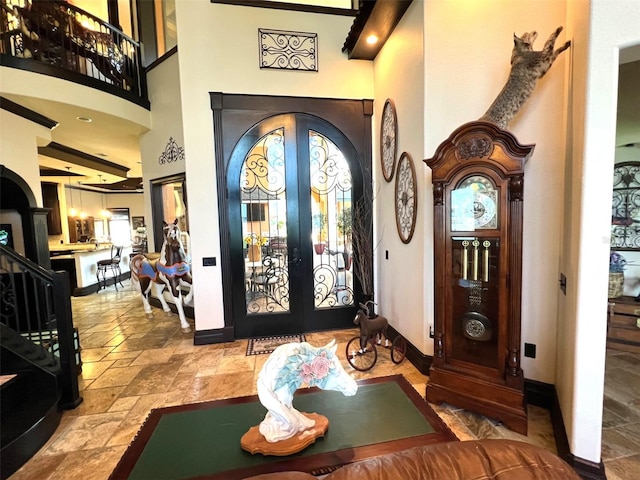 entrance foyer featuring arched walkways, a towering ceiling, baseboards, french doors, and stone tile flooring