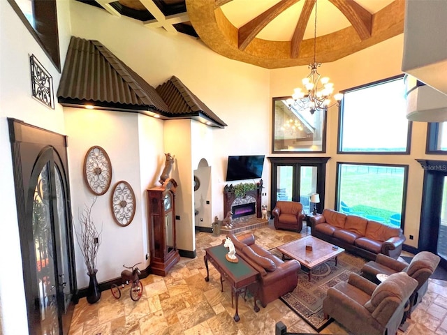 living area with a high ceiling, coffered ceiling, baseboards, stone tile flooring, and an inviting chandelier