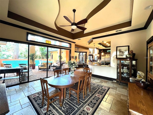 dining area with a raised ceiling, stone tile floors, baseboards, and a ceiling fan