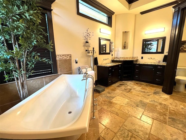 full bath with stone tile flooring, vanity, a freestanding bath, and toilet