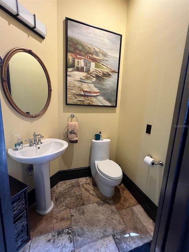 bathroom featuring toilet, stone finish floor, baseboards, and a sink