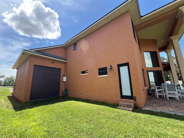 back of property featuring stucco siding, a patio, an attached garage, and a yard