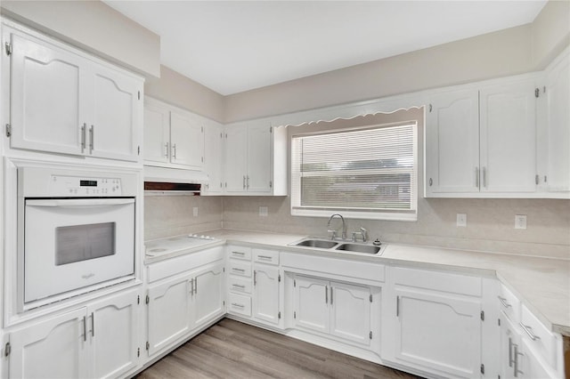 kitchen with backsplash, oven, light wood-type flooring, white cabinetry, and sink