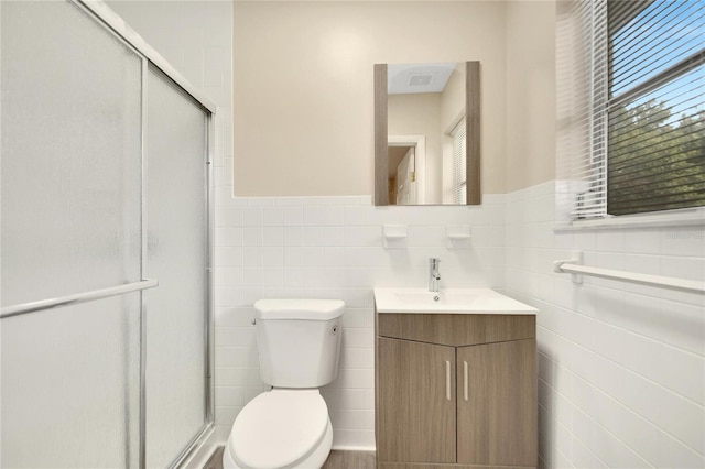 bathroom with toilet, vanity, tasteful backsplash, tile walls, and a shower with shower door