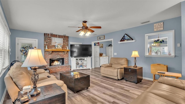 living area featuring ceiling fan, a wealth of natural light, a fireplace, and wood finished floors