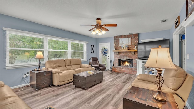 living area featuring light wood-type flooring, visible vents, a fireplace, and a textured ceiling