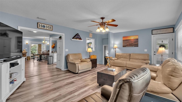 living room featuring light wood-style floors, visible vents, a textured ceiling, and ceiling fan with notable chandelier