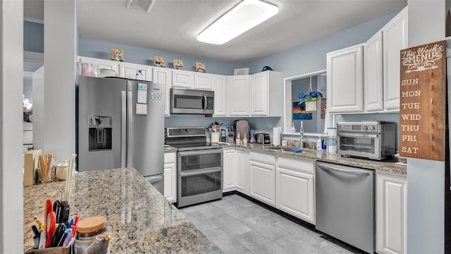 kitchen featuring light stone countertops, white cabinetry, stainless steel appliances, and a sink