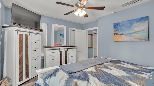 bedroom with a ceiling fan, wood finished floors, visible vents, and a barn door