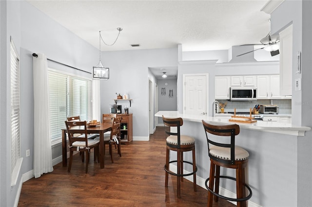 kitchen featuring ceiling fan with notable chandelier, kitchen peninsula, decorative backsplash, a kitchen bar, and white cabinetry