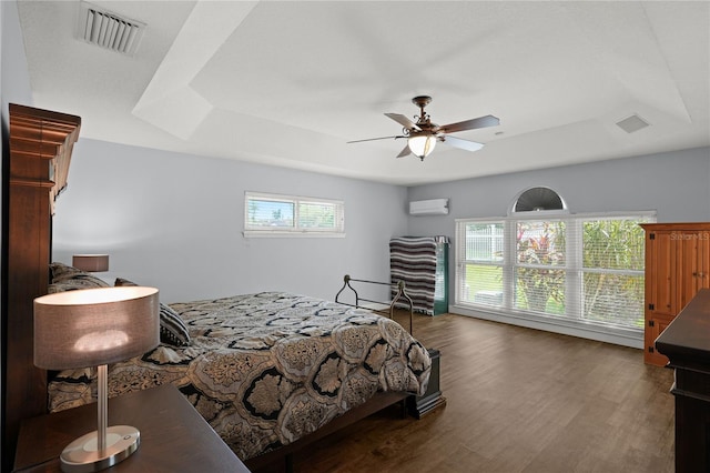 bedroom featuring dark hardwood / wood-style flooring, a raised ceiling, ceiling fan, and a wall unit AC