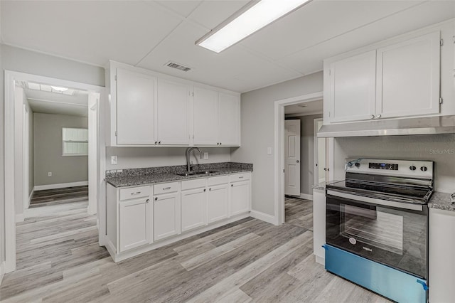 kitchen with light hardwood / wood-style floors, stainless steel electric stove, white cabinets, dark stone counters, and sink