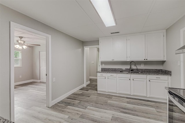 kitchen with light hardwood / wood-style floors, white cabinetry, ceiling fan, dark stone counters, and sink