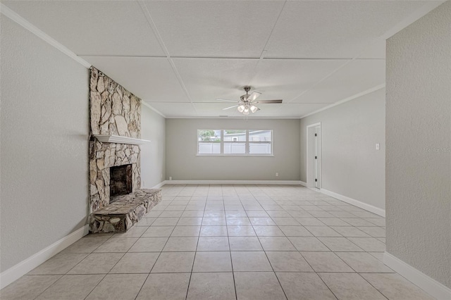 unfurnished living room featuring crown molding, a stone fireplace, light tile patterned flooring, and ceiling fan