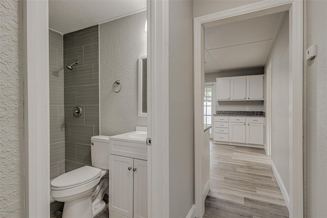 bathroom featuring a textured ceiling, hardwood / wood-style flooring, tiled shower, vanity, and toilet