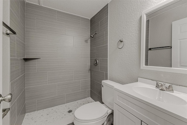 bathroom with vanity, toilet, a textured ceiling, and tiled shower