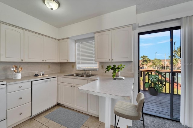 kitchen with white dishwasher, white cabinets, sink, tasteful backsplash, and light tile patterned flooring