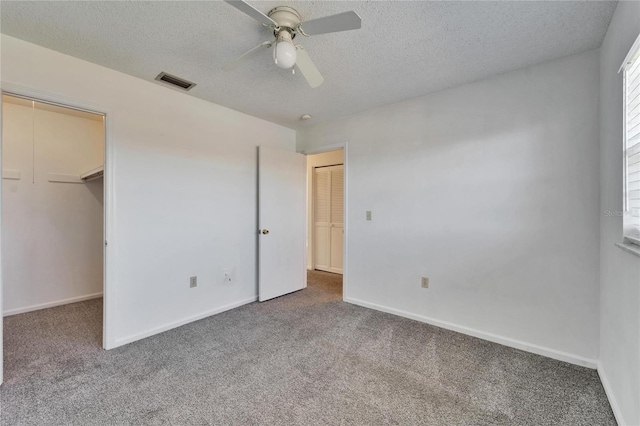 unfurnished bedroom with carpet flooring, a textured ceiling, ceiling fan, a spacious closet, and a closet