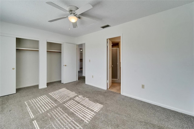 unfurnished bedroom with light carpet, a textured ceiling, two closets, and ceiling fan