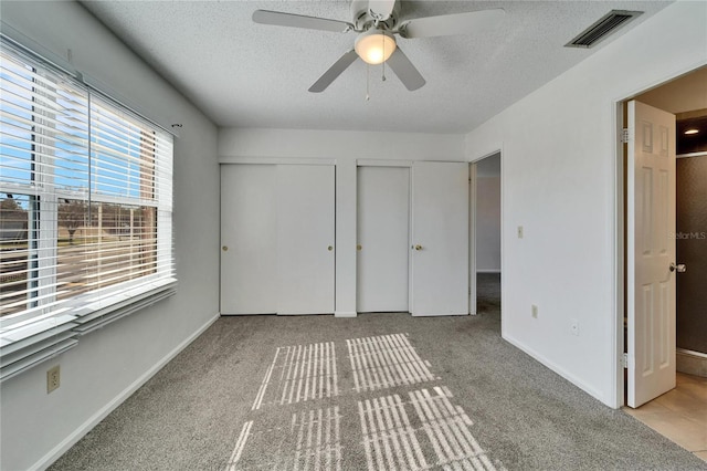 unfurnished bedroom with a textured ceiling, ceiling fan, light carpet, and two closets