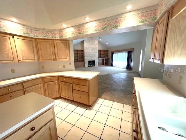 kitchen with light brown cabinetry, a stone fireplace, sink, and vaulted ceiling