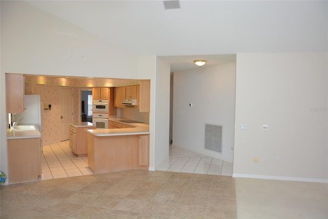 kitchen with vaulted ceiling, kitchen peninsula, light brown cabinets, light tile patterned floors, and sink