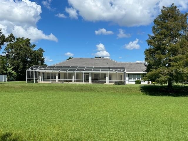 rear view of house featuring a lawn and glass enclosure