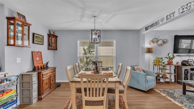 dining space with a textured ceiling, light hardwood / wood-style flooring, and a notable chandelier